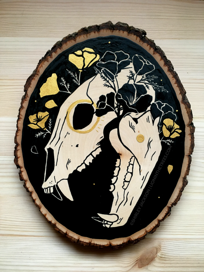 A painting on a wood slice featuring a bear skull against a black background with golden poppies entangled around the skull.