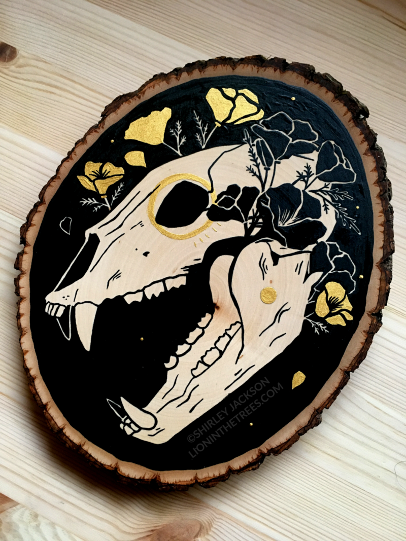 A painting on a wood slice featuring a bear skull against a black background with golden poppies entangled around the skull.