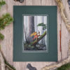 Photo of the matted artwork on a wood table with fir tree branches and wood