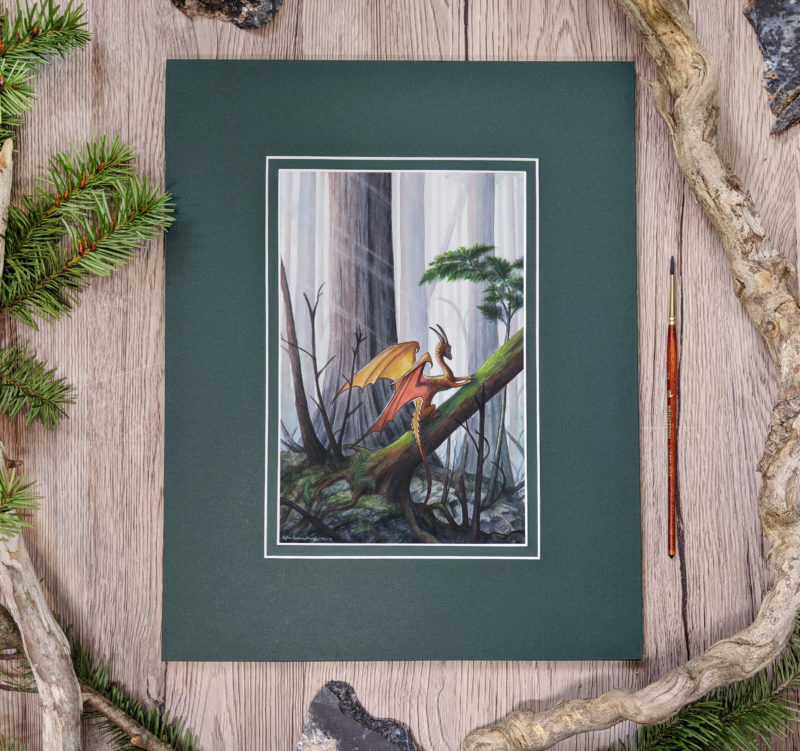 Photo of the matted artwork on a wood table with fir tree branches and wood