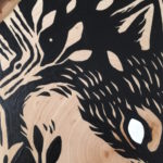 A painting on a wood slice featuring a wolf encircled within branches. It is diving down, in the center of the piece, with it's mouth open.