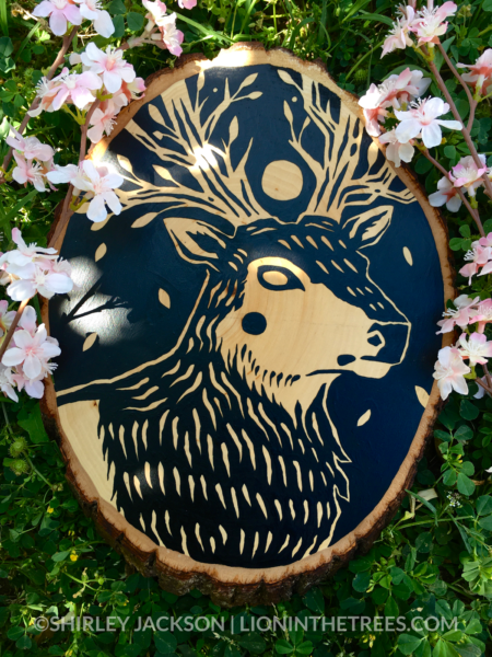 A painting on a wood slice featuring a featuring an elk with tree-like antlers and a full moon as a crown.