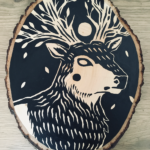 A painting on a wood slice featuring a featuring an elk with tree-like antlers and a full moon as a crown.