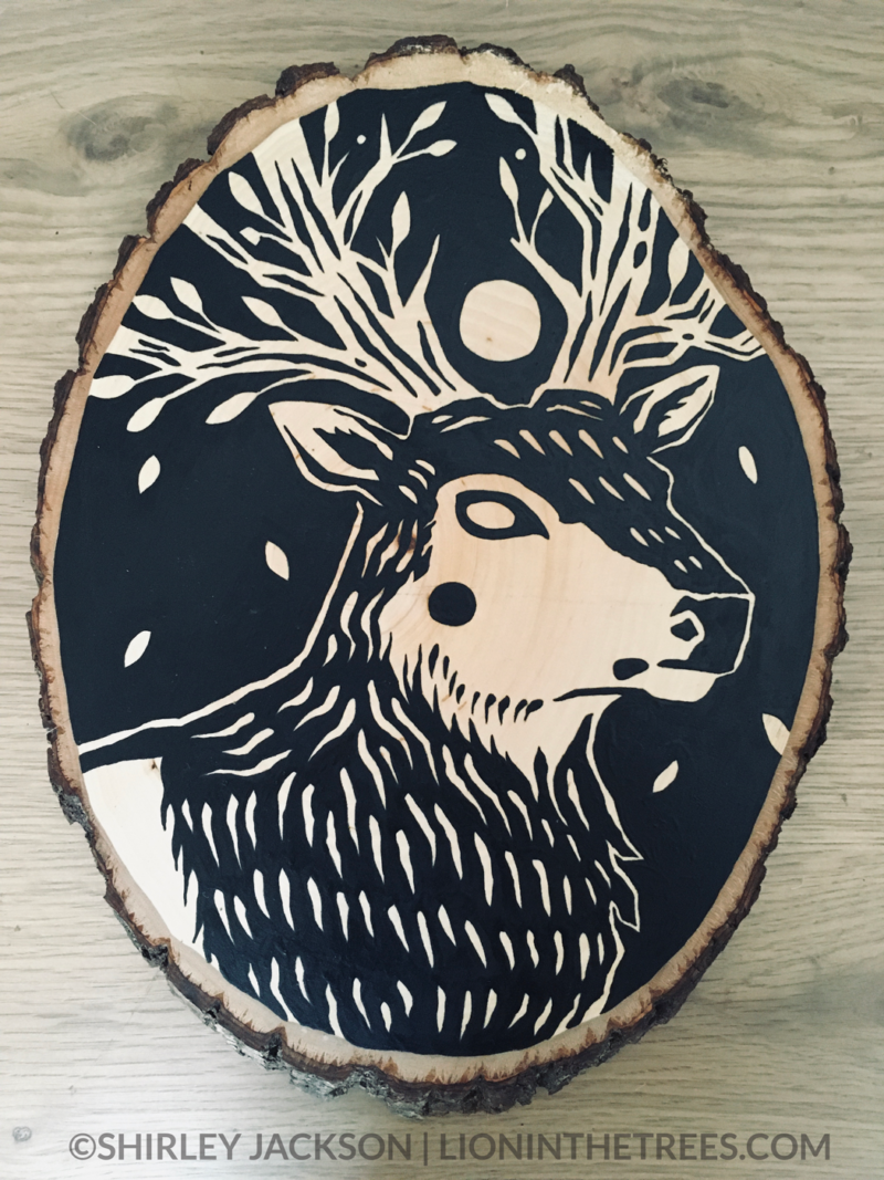 A painting on a wood slice featuring a featuring an elk with tree-like antlers and a full moon as a crown.