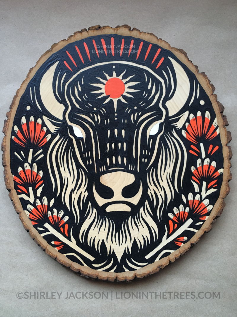 A painting on a wood slice featuring an American Bison with a red sun symbol on its forehead. It is also surrounded by Indian Paintbrush aka Prairie-Fire plants on either side.