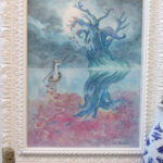 Painting The Journey Home with an white carved wooden frame. There is a white jar on the right and some brushes on the bottom.