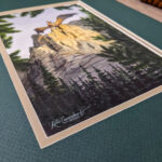 Golden Hour dragon standing on a cliff with wings out above a forest painted in watercolor corner photo showing signature up close