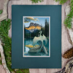 A pale greenish blue dragon perches on a tree in a lake, facing the mountain range as the sun sets across it