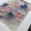 Pictured is a watercolor painting of three overlapping skulls floating amidst rich watercolor washes.