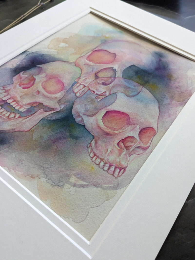 Pictured is a watercolor painting of three overlapping skulls floating amidst rich watercolor washes.