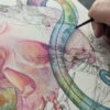 A watercolor painting of a rainbow snake wrapping around a human skull. There are sketchy ink humming birds overlaying the painting.