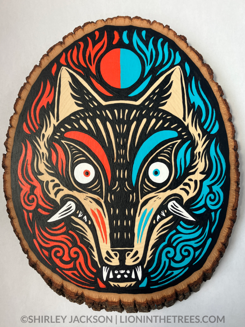 A painting on a wood slice featuring a coyote head. The left side is coloured with red details, and the right side is coloured with light blue details.