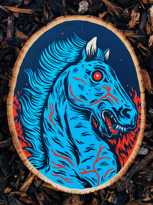 A painting on a wood slice featuring Blucifer, the blue demon mustang statue that is outside of the Denver Airport. He has red fire-y flames of hell on either side of him.