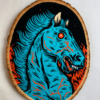 A painting on a wood slice featuring Blucifer, the blue demon mustang statue that is outside of the Denver Airport. He has red fire-y flames of hell on either side of him.