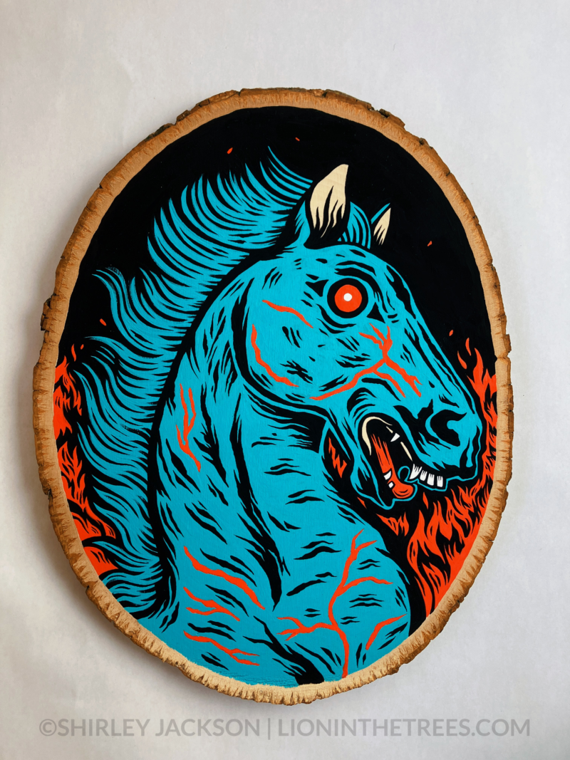 A painting on a wood slice featuring Blucifer, the blue demon mustang statue that is outside of the Denver Airport. He has red fire-y flames of hell on either side of him.