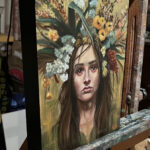 painting on easel of woman in floral headdress in colors of autumn: gold, olive, red, brown