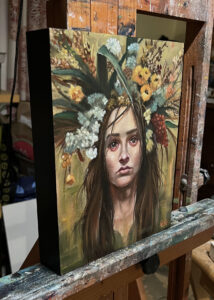 painting on easel of woman in floral headdress in colors of autumn: gold, olive, red, brown