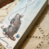 Side view image of painting of playful rat holding blue string with teal beads around the floor