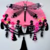 A shiny black dragonfly rests on a bright pink vintage fan decorated with a lot of fringe, beads and cascading flowers