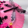 Detail of shiny black dragonfly rests on a bright pink vintage fan decorated with a lot of fringe, beads and cascading flowers