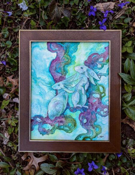 A watercolor painting of two bunnies sitting on purple roots. It is framed, surrounded by leaves from outdoors.