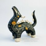 Sgraffito dragon totem done with black and orange underglazes, and finished with gold overglaze in some areas. The dragon has it's head reared up and California Poppies have been carved into it's side along with other markings. This photo shows the left side of the sculpture.