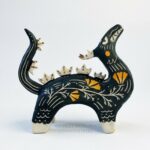 Sgraffito dragon totem done with black and orange underglazes, and finished with gold overglaze in some areas. The dragon has it's head reared up and California Poppies have been carved into it's side along with other markings. This photo shows the right side of the sculpture.