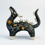 Sgraffito dragon totem done with black and orange underglazes, and finished with gold overglaze in some areas. The dragon has it's head reared up and California Poppies have been carved into it's side along with other markings. This photo shows the left side of the sculpture.