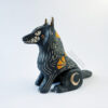 Sgraffito wolf totem done with black and orange underglazes, and finished with gold overglaze in some areas. The wolf is sitting down and California Poppies have been carved into it's side along with other markings. There are also crescent moon details done in gold overglaze. This photo shows the 3/4 left front view.