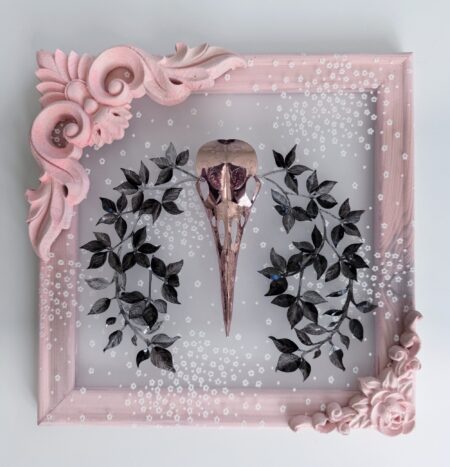 Pink metallic filigreed crow skull surrounded by black leaves