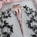 Detail of pink metallic filigreed crow skull surrounded by black leaves