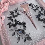 Detail of pink metallic filigreed crow skull surrounded by black leaves