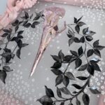 Detail of pink metallic filigreed crow skull surrounded by black leaves