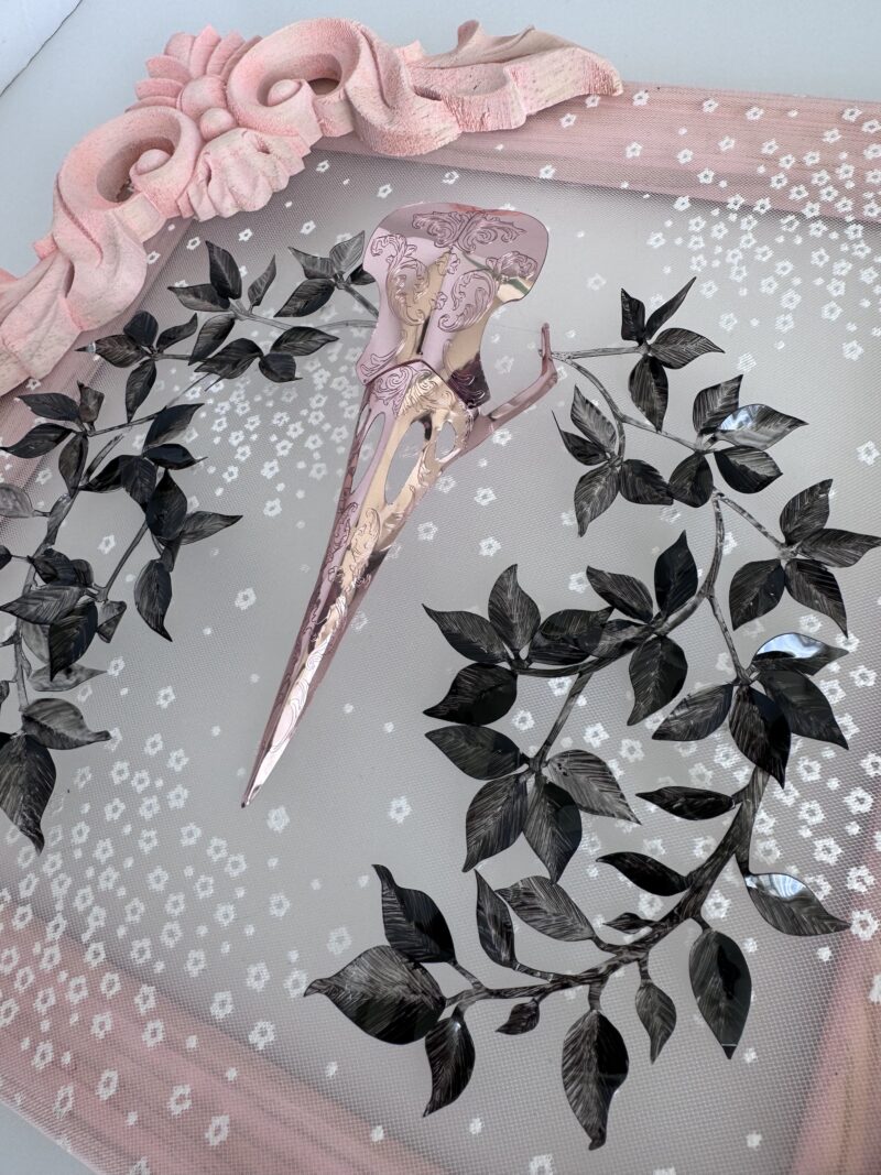 Detail of pink metallic filigreed crow skull surrounded by black leaves