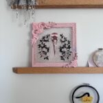 Pink metallic filigreed crow skull surrounded by black leaves on shelf