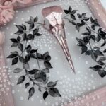 Detail of pink metallic filigreed crow skull surrounded by black leaves
