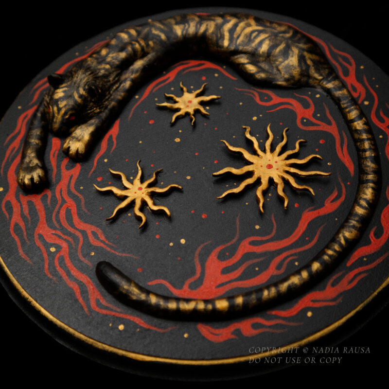 A relief sculpture of a tiger surrounded by flames and stars on a round wooden board against a dark background.