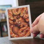 A portrait of a Gorgon smiling. The snakes are orange-color pythons. She has brown skin and has a lovely smile on her face.