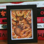 A portrait of a Gorgon smiling. The snakes are orange-color pythons. She has brown skin and has a lovely smile on her face.