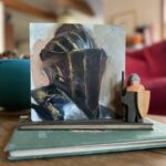 Greg Mancjess painting of a 1500s Nerumberg Jousting helm on top of a stack of books next to a wooden toy knight