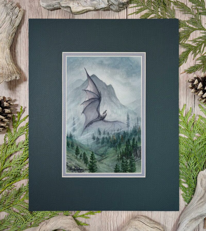 A dark gray dragon rises up through the foggy forested hillside with a mountain and cloudy sky in the background. Photo shows artwork in the mat it will come in.