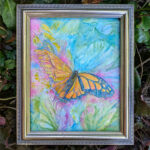 Photo of a butterfly painting. It is framed in pale gold and surrounded by leaves outside. The butterfly is a bright orange monarch.