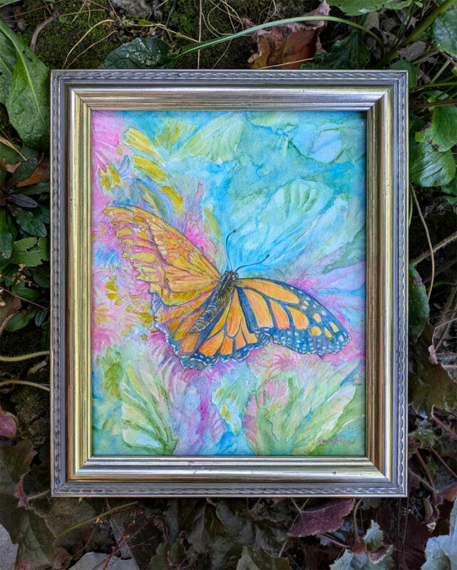 Photo of a butterfly painting. It is framed in pale gold and surrounded by leaves outside. The butterfly is a bright orange monarch.
