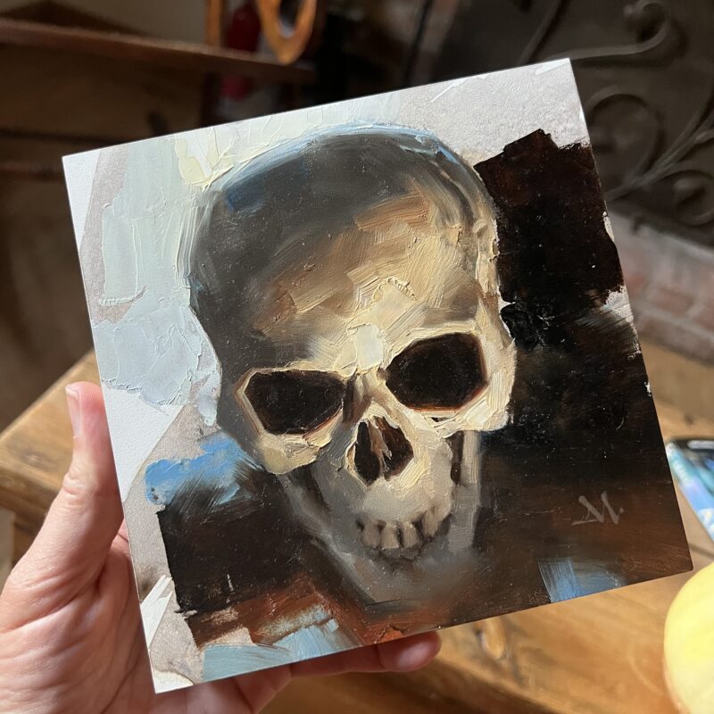 A hand holding up an oil painting of a skull by Greg Manchess.