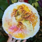 "Autumn Fae" by Laura Garabedian - watercolor painting of a fae woman's portrait in profile with curlly auburn hair looking side eye at the viewer on an abstracted background of golds and pinks
