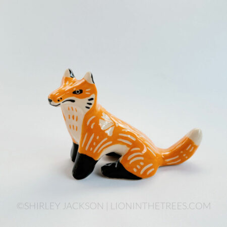 Sgraffito fox totem done with orange and black underglazes that mimics that colour pattern of a real fox. Finished with a clear glaze and carved California Poppies and various markings all over it's body. This is a left-side view of the piece.