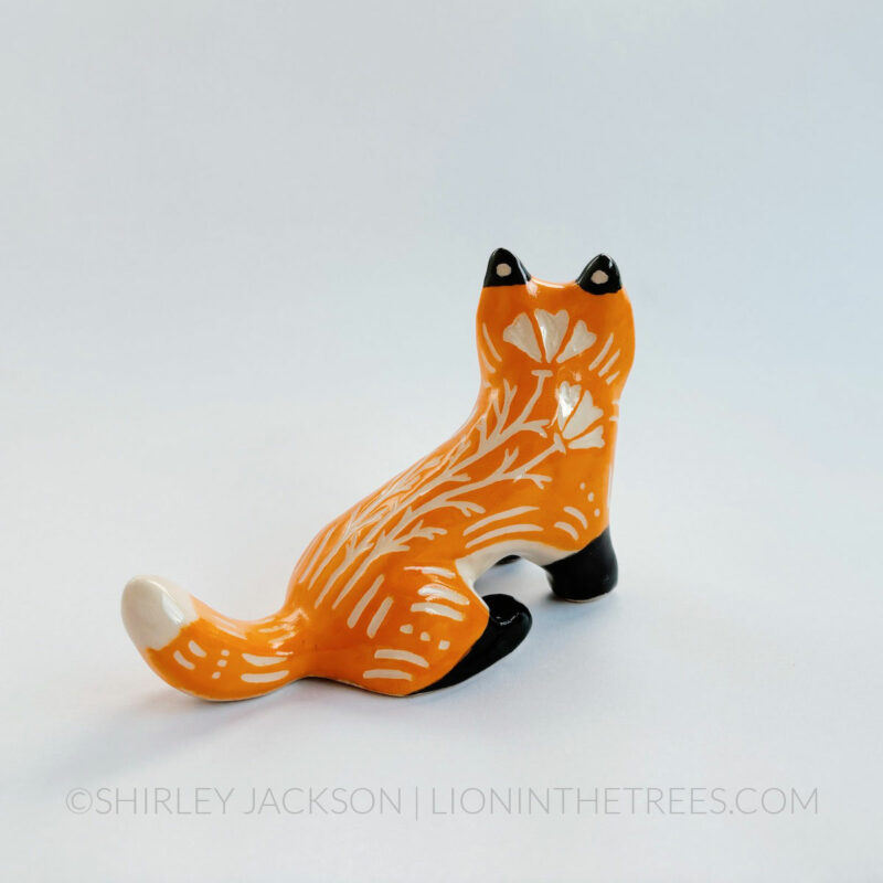 Sgraffito fox totem done with orange and black underglazes that mimics that colour pattern of a real fox. Finished with a clear glaze and carved California Poppies and various markings all over it's body. This is the backside/right side view that shows more of the poppies.