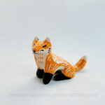 Sgraffito fox totem done with orange and black underglazes that mimics that colour pattern of a real fox. Finished with a clear glaze and carved California Poppies and various markings all over it's body. This is a front view of the piece.