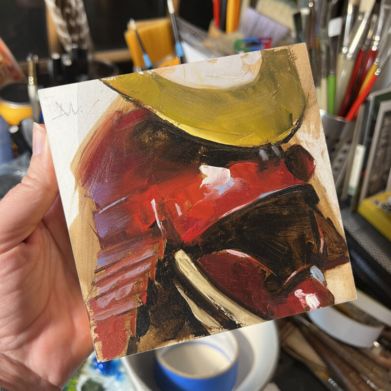 A hand holding a 5 x 5 oil painting of a red Samurai helmet by Greg Manchess.