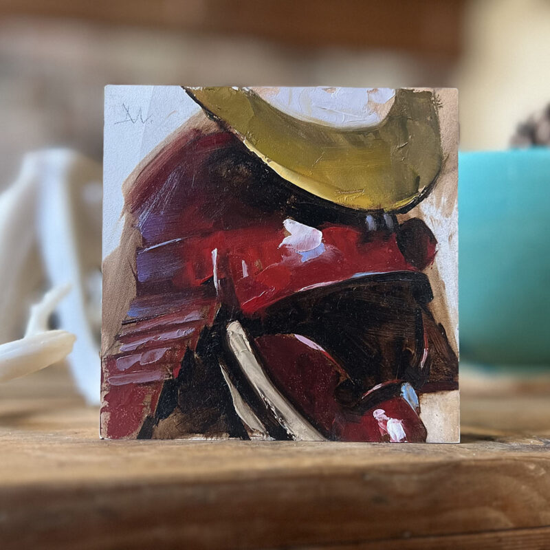 A 5 x 5 oil painting of a Samurai helmet by Greg Manchess sitting on a desk.